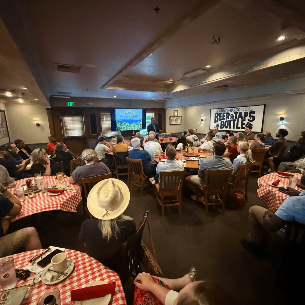 A packed Money 101 seminar at a BBQ restaurant — red checkered tablecloths, full room of attendees, screen in the background. The real room.